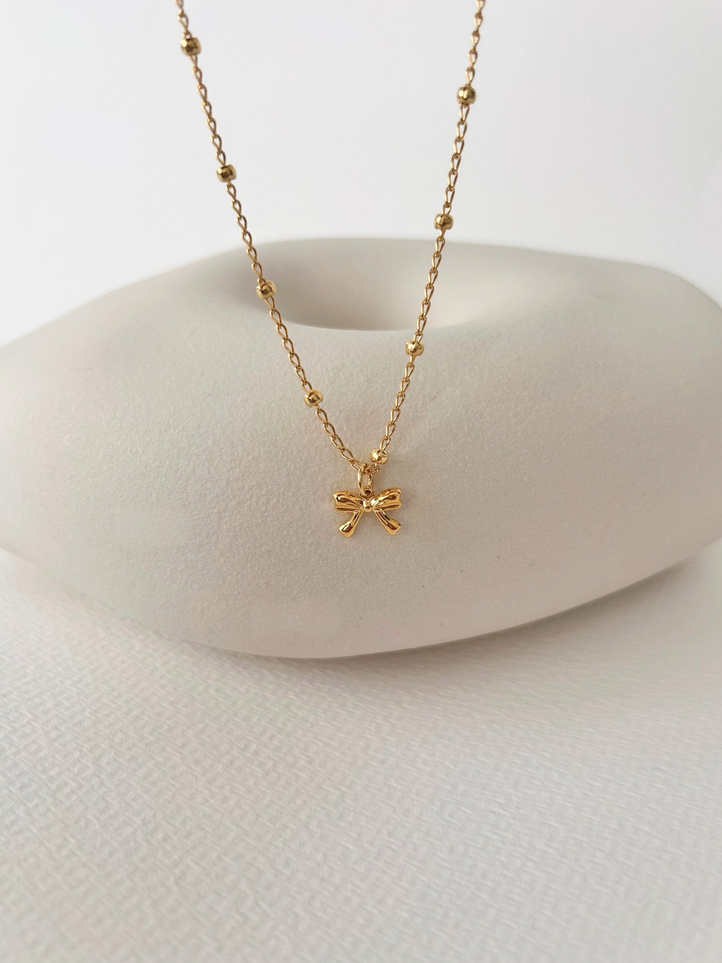 Choker con lazo en oro laminado (gold filled) 18K. Delicado y duradero, con estilo coquette para un toque femenino y juguetón. Collar corto ajustable con dije. Cadena con cuentas, tipo satélite. Regalo romántico para ella, Trópico Jewelry
