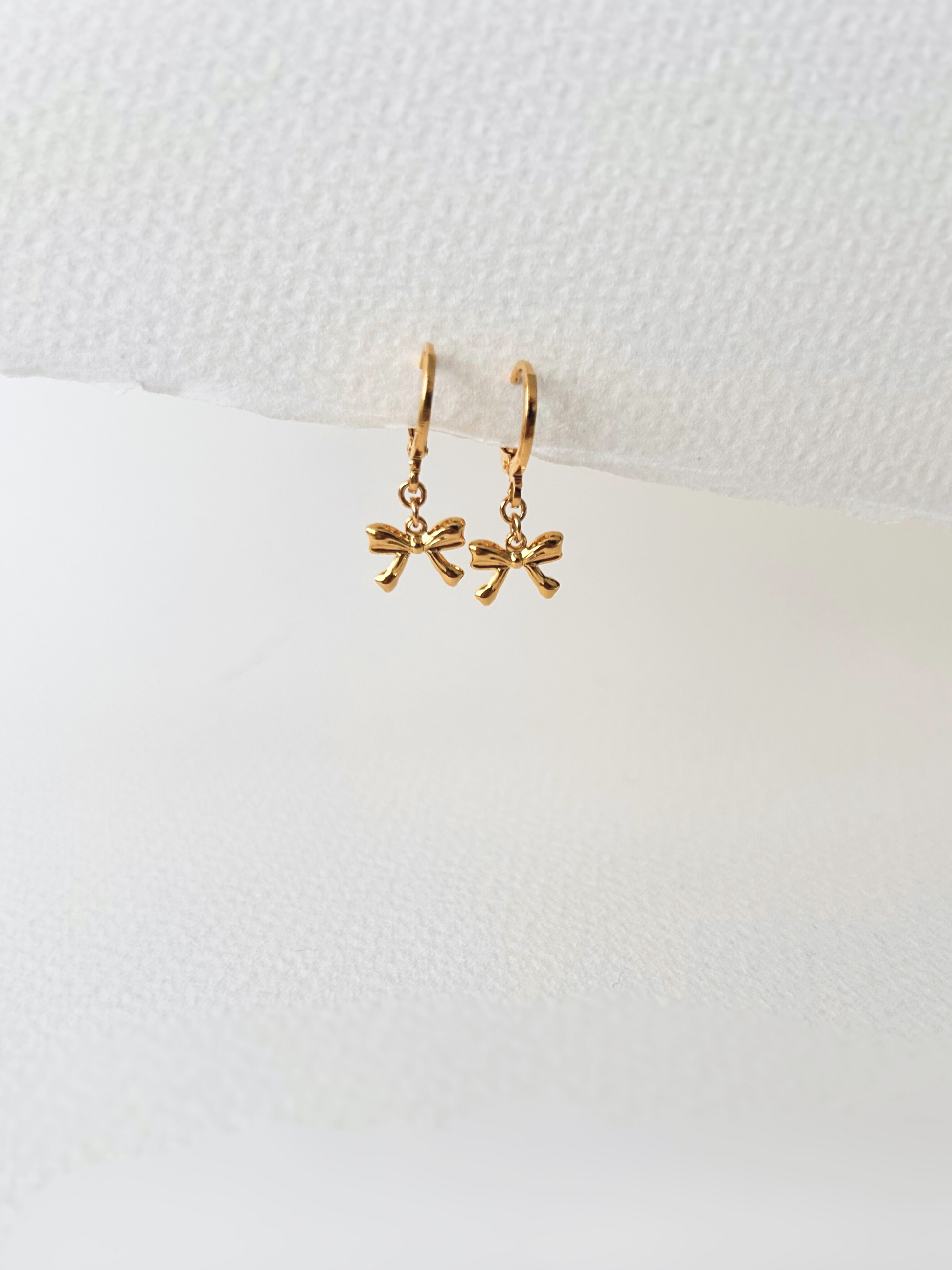 Pendientes de argollas con lazos en oro laminado 18K (gold filled). De estilo coquette, son muy femeninos y favorecedores. Duraderos, resistentes al agua y perfectos para el uso diario. Son ideales como un regalo delicado para mujer. Trópico Jewelry.