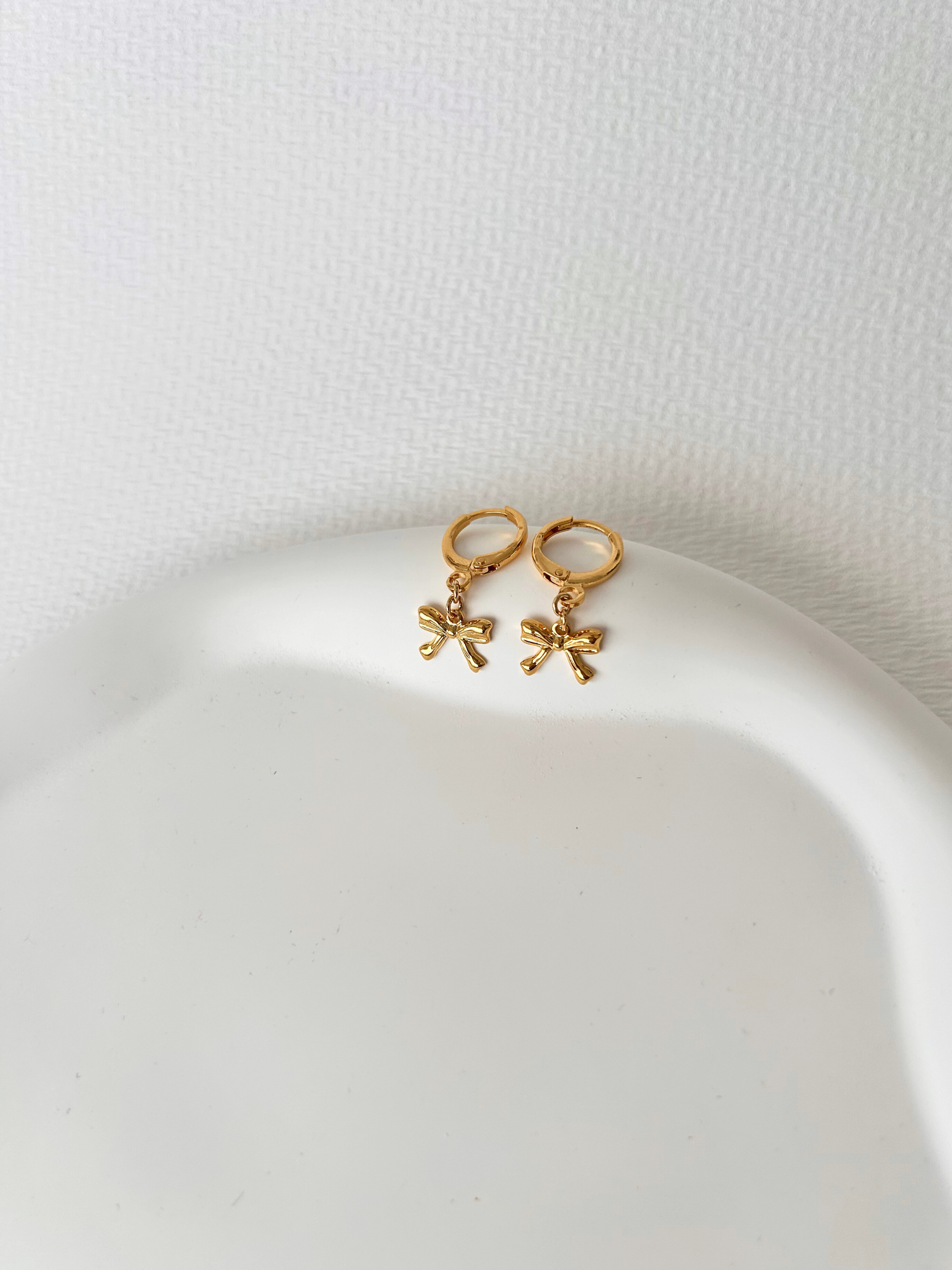 Pendientes de argollas con lazos en oro laminado 18K (gold filled). De estilo coquette, son muy femeninos y favorecedores. Duraderos, resistentes al agua y perfectos para el uso diario. Son ideales como un regalo delicado para mujer. Trópico Jewelry.